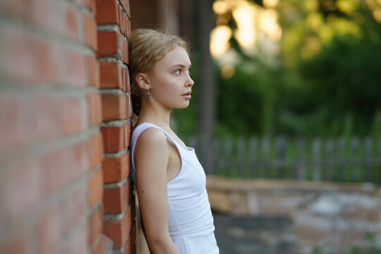 Girl in a white dress standing by a brick wall and fence outdoors