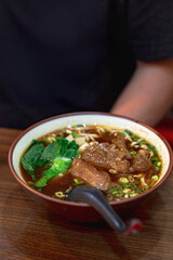 Bowl of Taiwanese braised beef noodle soup with rich broth, tender beef chunks, fresh greens, and noodles, served in a cozy local eatery