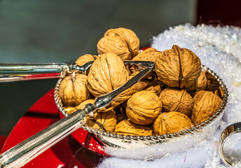 Decorative bowl filled with whole walnuts surrounded by festive decorations and serving tongs during a holiday celebration