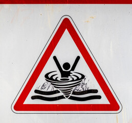 Warning sign indicating danger of drowning in a water body with whirlpool graphic in a public area
