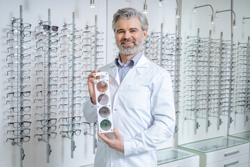 Male doctor in the optic shop holding a lens color scale in hands