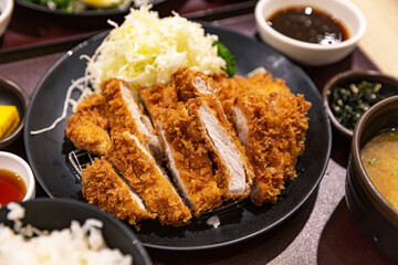 Japanese loin katsu set meal with crispy pork loin cutlet, shredded cabbage, dipping sauce, miso soup, and pickled vegetables on a dark serving tray
