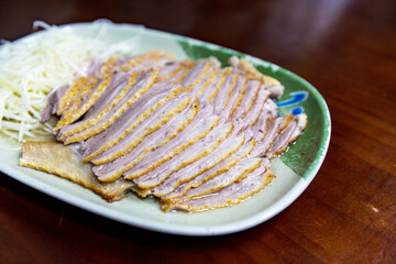 Close-up of Taiwanese smoked goose with juicy slices and visible sheen, served with scallions on a traditional plate