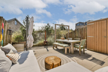 A serene outdoor patio featuring comfortable seating, a wooden table, and lush greenery, ideal for relaxation and gatherings. The scene is bright and inviting.