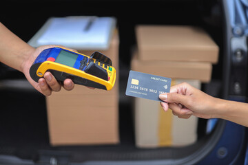 Close Up Of Hands Doing Transaction With EDC Machine And Credit Card Near Parcels In Car Trunk