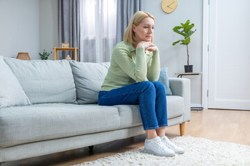 Pretty mid aged blonde woman sitting on the sofa and looking contented