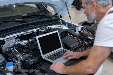 Engineer bearded man looking at inspection vehicle details under car hood using laptop