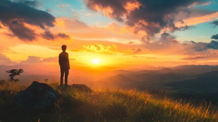 Obraz premium Silhouette of a man standing on a hilltop, watching the sunset.