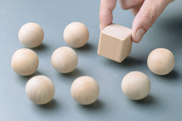 A man's hand is placing a wooden cube among many wooden balls,  concept of positioning in a...