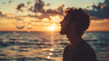 Silhouette of a man watching soap bubbles float in the air at sunset by the ocean
