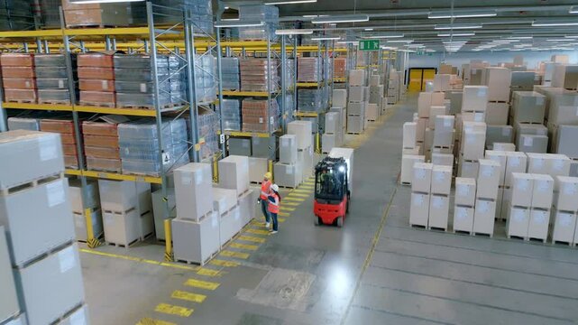 A bird's-eye view of a bustling warehouse reveals workers navigating aisles, forklifts transporting cargo, and shelves brimming with packages, symbolizing efficiency and coordination in logistics.