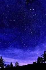 Fototapeta premium Enchanting nightscape of starry sky over silhouette trees and hill creating a serene and magical atmosphere with a person sitting on a bench under the vast cosmos