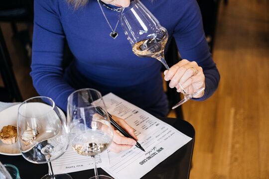 Woman filling out a wine tasting card while holding a wine glass at a communal table. Wine workshop, food and wine pairing, experiential education, sensory analysis