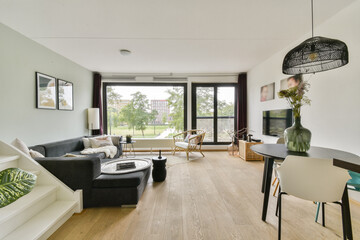 A sleek, modern living room featuring a stylish sofa, wooden flooring, and large windows with a view of greenery outside.