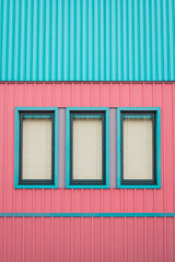 Fototapeta premium three windows with beige blinds on a pink and teal building
