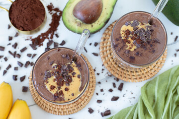 Chocolate avocado smoothie with cocoa powder, peanut butter, and banana on white kitchen table. Top...