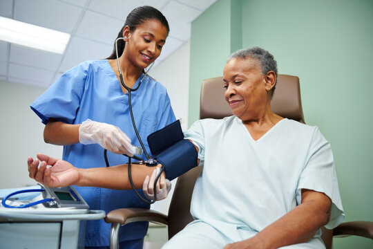Female nurse taking blood pressure of elderly african female patient in hospital