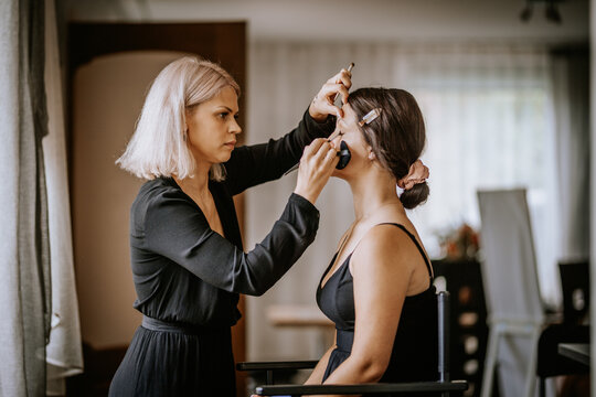 Makeup artist applying bridal makeup on a woman before the wedding ceremony in a softly lit indoor space..