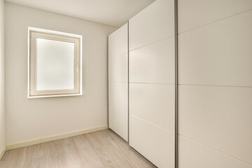 A contemporary room featuring a sleek wardrobe and a window allowing soft natural light, exemplifying minimalist interior aesthetics.