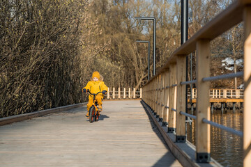 A cute boy in bright yellow clothes rides a bike. A happy child plays outside in early spring....