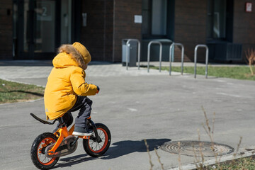 A cute boy in bright yellow clothes rides a bike. A happy child plays outside in early spring....