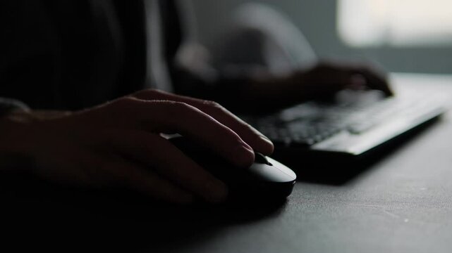 Close-up of man hand using a computer mouse in home office setup, highlighting remote work process and focused freelancing routine in natural low light environment