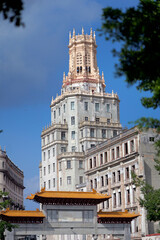 A historic ornate tower rises above the trees in Havana’s Chinatown (Barrio Chino), Cuba. The architecture blends neo-Gothic and Moorish elements with intricate stonework and slender arched windows.
