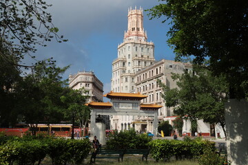 A historic ornate tower rises above the trees in Havana’s Chinatown (Barrio Chino), Cuba. The architecture blends neo-Gothic and Moorish elements with intricate stonework and slender arched windows.
