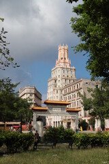 A historic ornate tower rises above the trees in Havana’s Chinatown (Barrio Chino), Cuba. The architecture blends neo-Gothic and Moorish elements with intricate stonework and slender arched windows.
