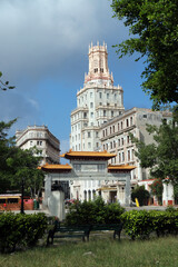 A historic ornate tower rises above the trees in Havana’s Chinatown (Barrio Chino), Cuba. The architecture blends neo-Gothic and Moorish elements with intricate stonework and slender arched windows.
