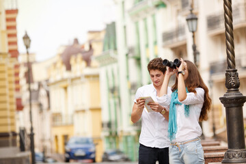 Man and woman traveling through the beautiful old city of Europe. Happy couple tourists with map and binoculars, a walk through the historic center of the city. Summer holidays, love and relationship.