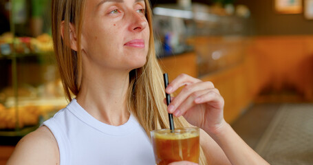 Woman enjoys iced coffee with straw in cozy cafe with blurred background