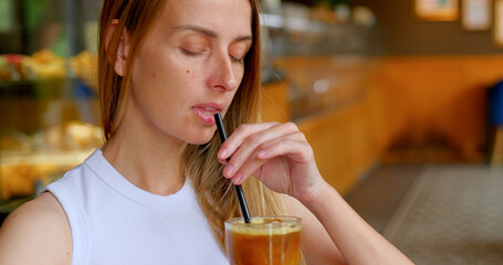 Woman enjoys iced coffee with straw in cozy cafe with blurred background