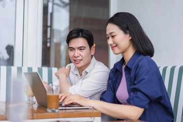 Young Asian couple enjoying coffee while working on a laptop in a cozy cafe during the afternoon