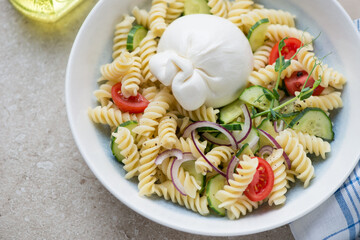 Fusilli pasta with burrata cheese and vegetables in a white and blue plate, horizontal shot on a...
