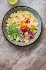 Rustic plate with farfalle pasta salad on a dark-brown granite background, vertical shot with space, above view