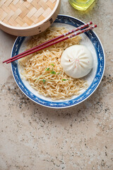 Blue and white plate with steamed asian baozi and noodles, vertical shot on a beige granite background with space, above view