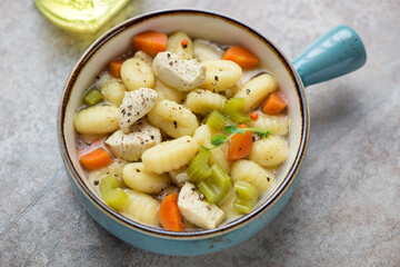 Chicken soup with italian potato gnocchi and vegetables in a turquoise serving bowl, horizontal shot on a brown granite background