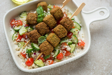Wooden skewers with falafel, couscous and vegetable salad in a beige serving tray, horizontal shot, middle close-up