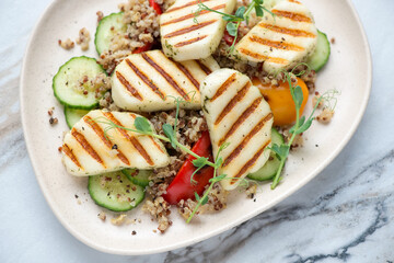 Grilled halloumi cheese with quinoa, bell pepper and cucumber on a beige plate, horizontal shot, middle closeup