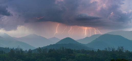 Lightning bolts strike across mountain ridges under dramatic storm clouds, capturing the power and beauty of nature during a thunderstorm over a forested landscape.