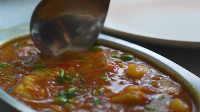 Closeup shot of man picking up aloo mutter curry from a bowl with the help of spoon. Delicious North Indian food background with copy space. Man pick up cooked vegetables with a big spoon.