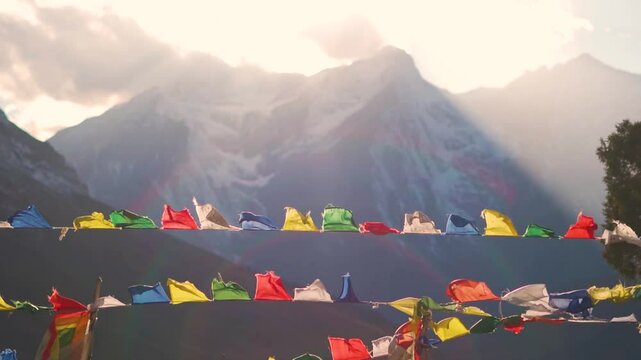 Slow motion shot of prayer flags waving in the wind in front of snowy Himalayan mountain peak with sun rays during the sunset as seen from Tayul Monastery near Keylong in Himachal Pradesh, India.