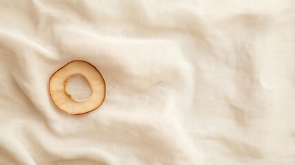 Close-up of a single slice of apple lying on a white fabric. the apple is cut in half, with the outer edge of the slice facing towards the right side of the image.