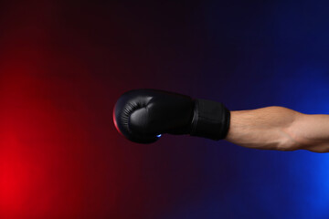 Man with boxing glove fighting on dark background in neon lights, closeup. Space for text