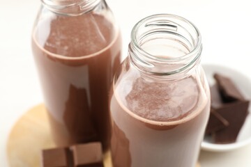 Tasty chocolate milk and pieces on white table, closeup