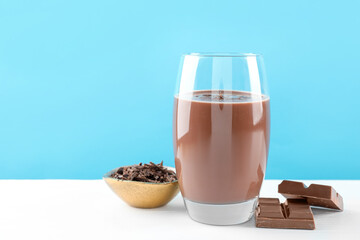 Tasty chocolate milk with shavings and pieces on white table against light blue background. Space for text