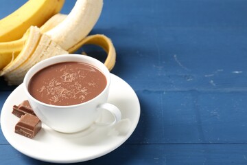 Tasty chocolate milk in cup, pieces and bananas on blue wooden table, closeup. Space for text