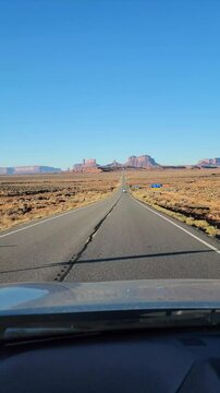 4K vertical high resolution mobile video of driving from Forrest Gump Point in Utah toward Monument Valley in Arizona, showing open desert road and scenic rock formations under blue sky