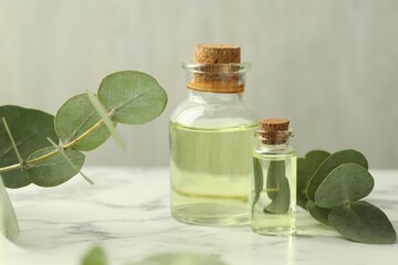 Bottles of essential oil and eucalyptus leaves on white marble table, closeup